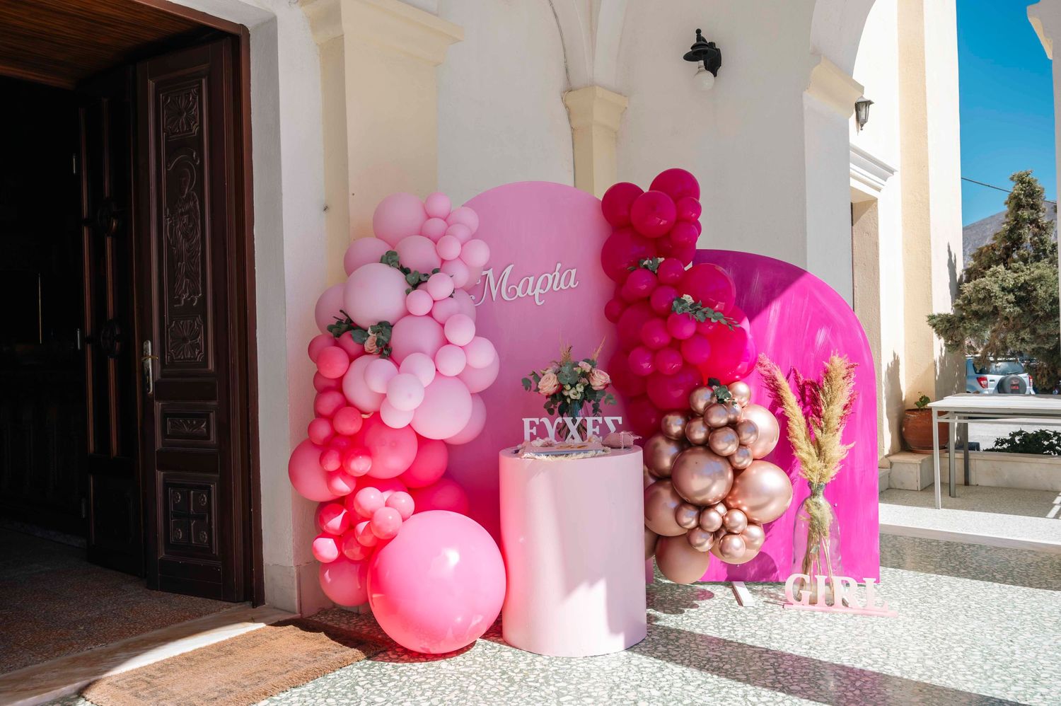 Pink and white balloon arch with floral decorations against church entrance.