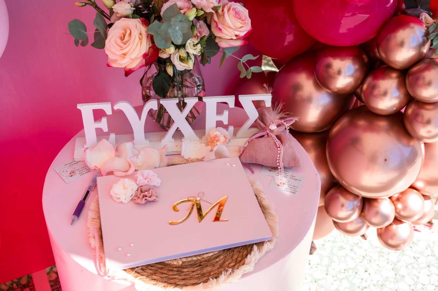 Elegant pink party setup with roses and rose gold balloons displaying text.