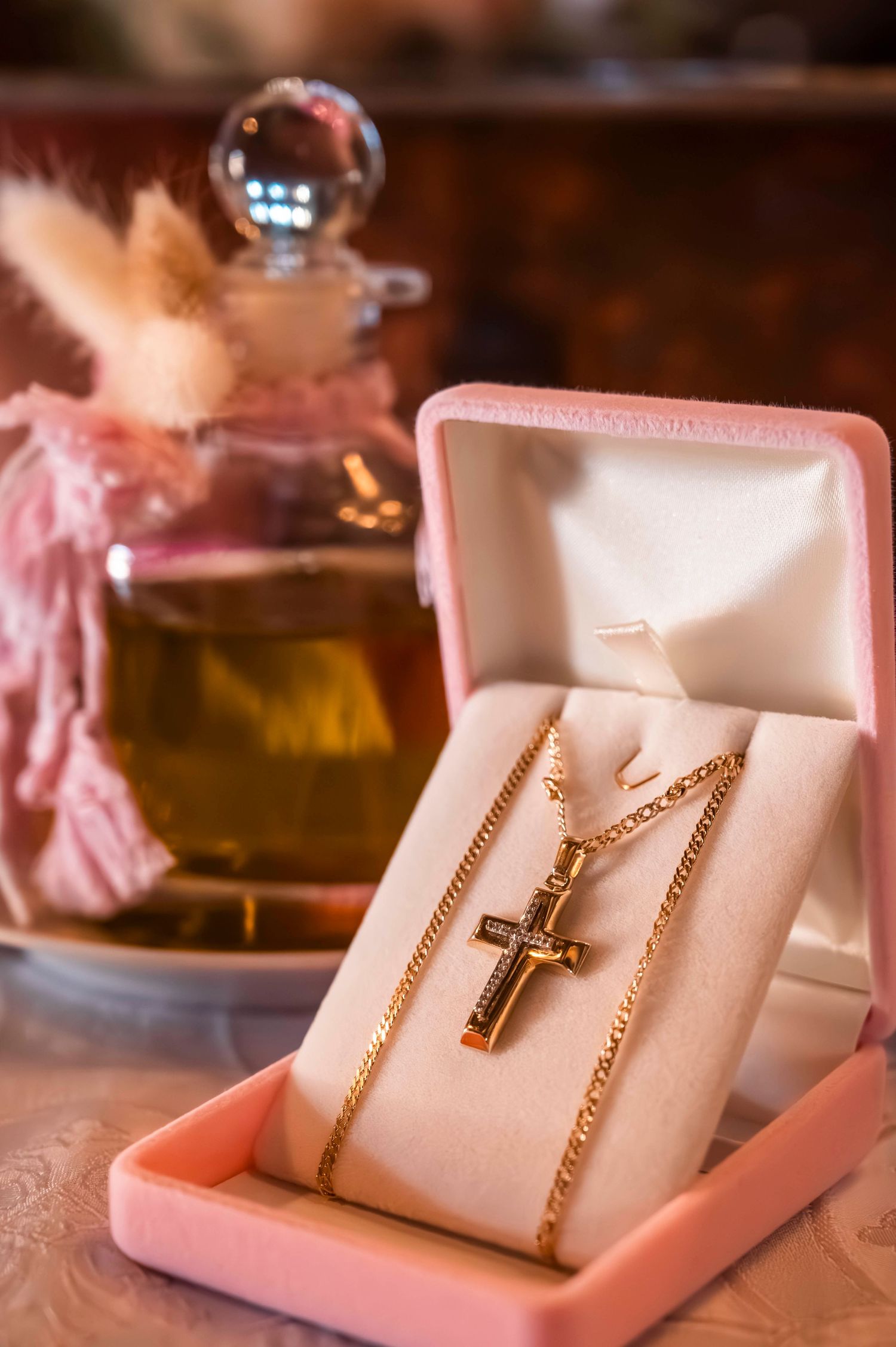 Golden crucifix necklace displayed in a pink jewelry box next to a decorative glass bottle.