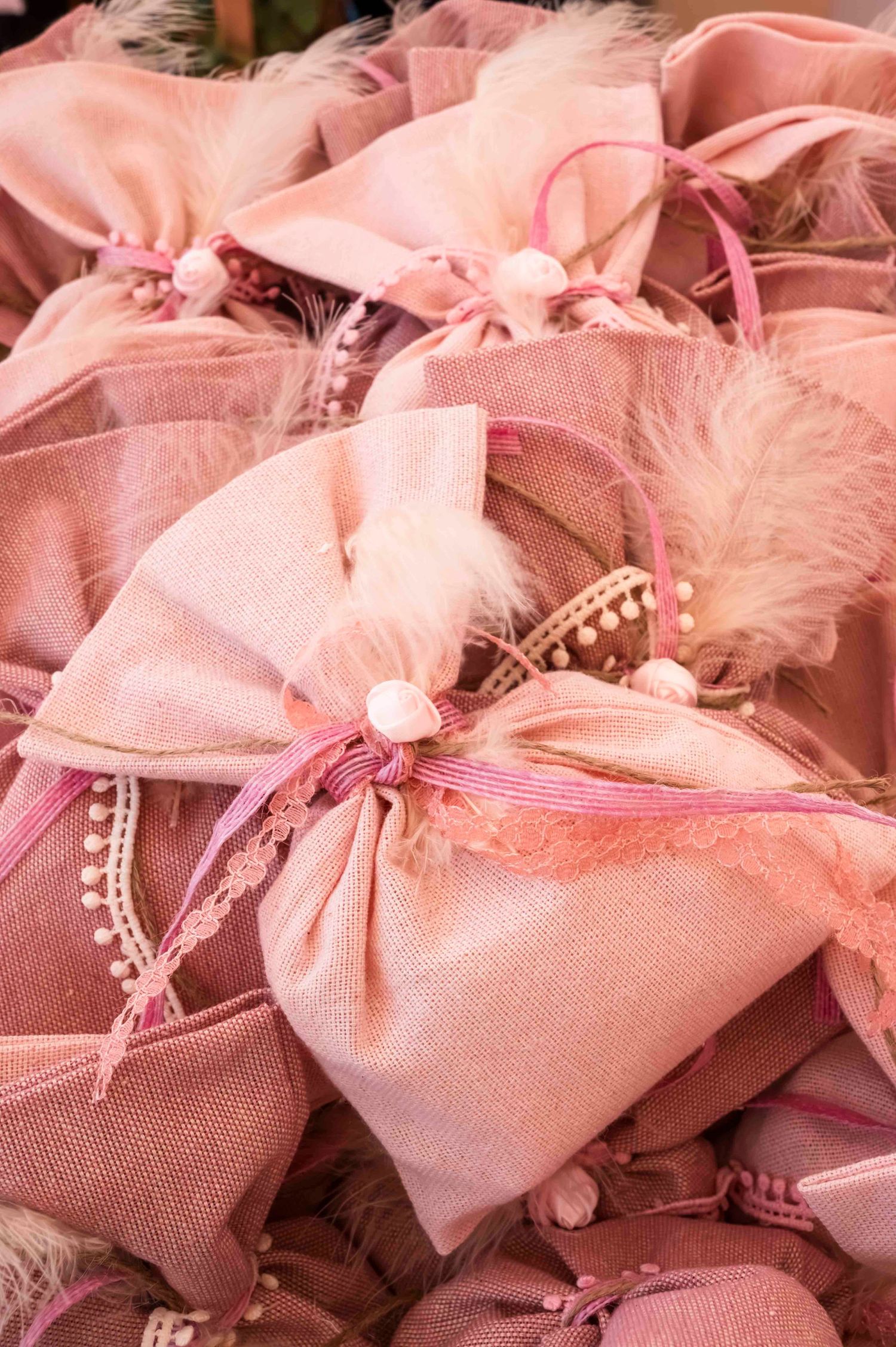 Pink satin favor bags with pearls and feathers arranged in a delicate pattern.