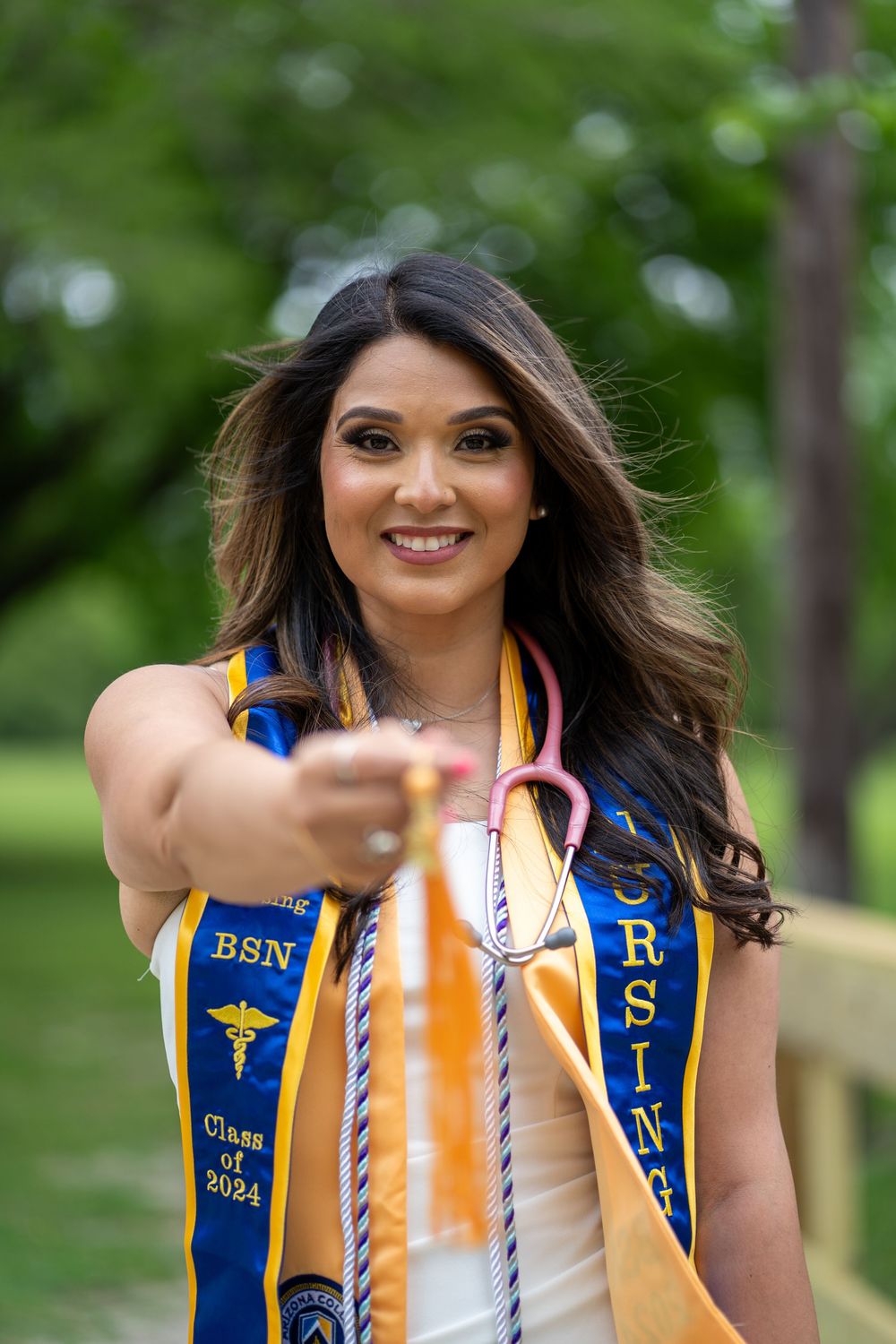 Nursing graduate wearing graduation stoles and cords poses outdoors.