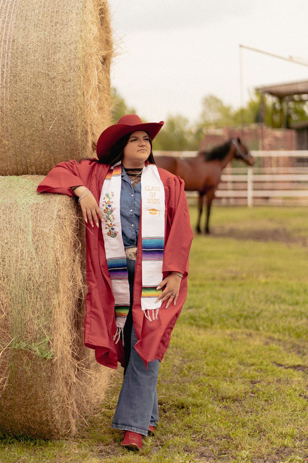 Country style portrait session near hay bales wearing a burgundy jacket.