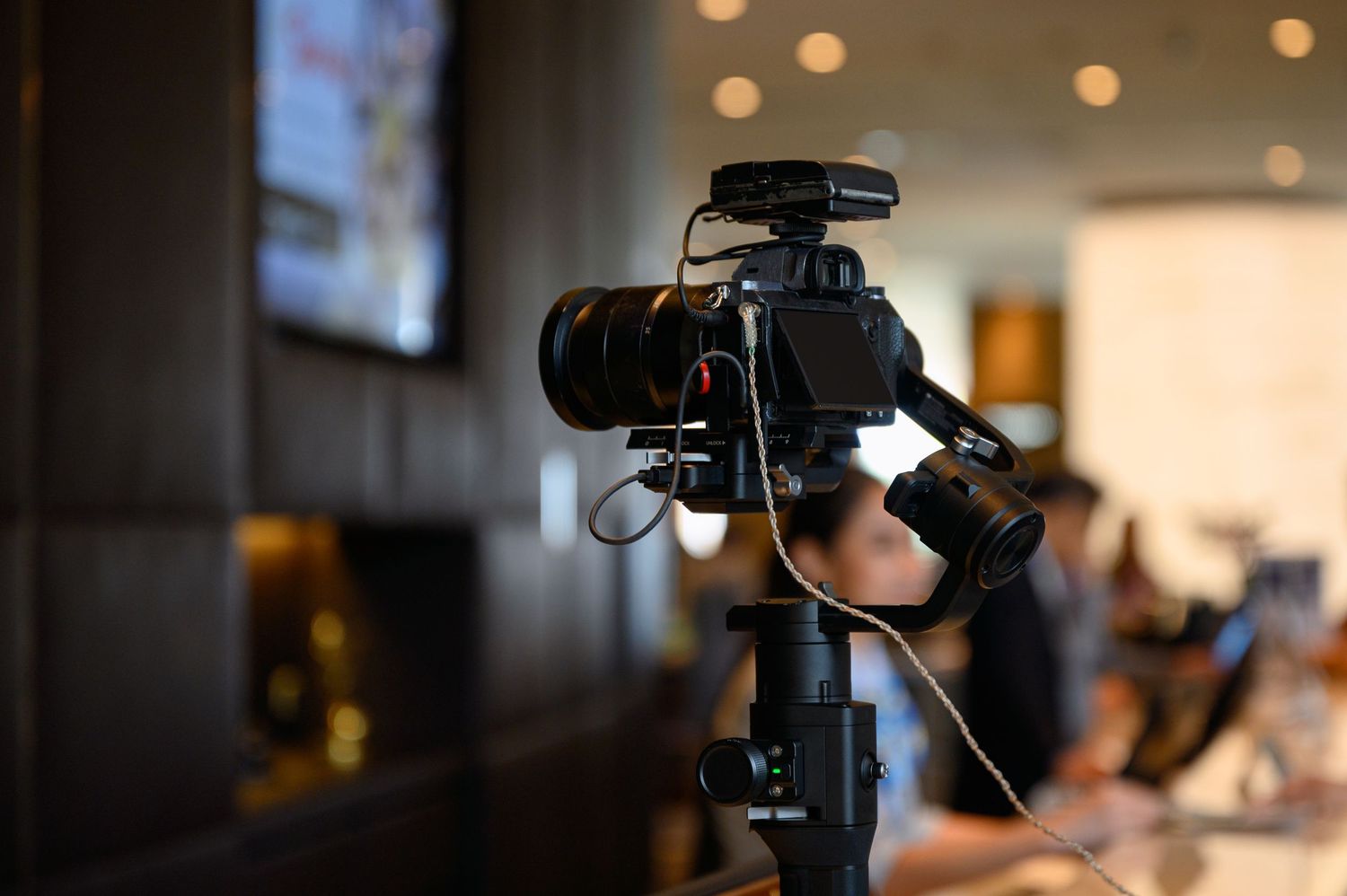 A close-up view of a professional video camera capturing footage at an indoor event with blurred bokeh lights.