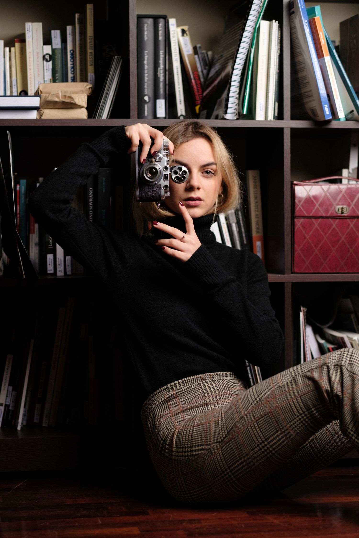 Artistic photo of person lounging near bookshelf with vintage camera.