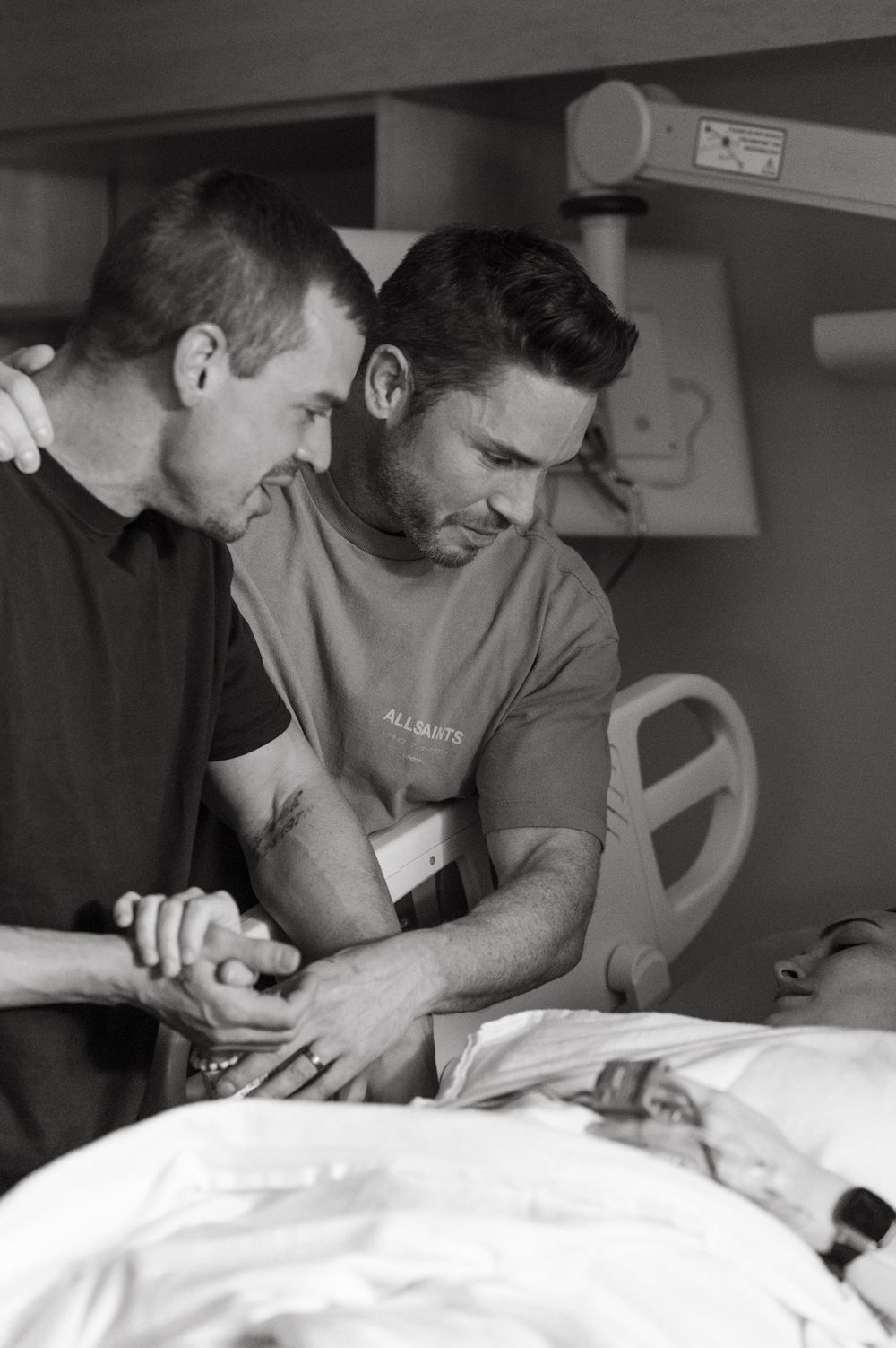 Black and white photo showing two medical professionals examining a patient on a hospital bed.