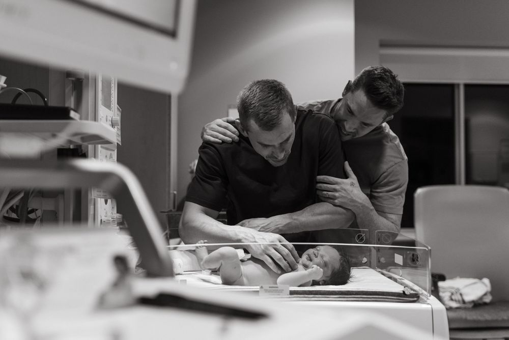 Two medical professionals check on a small baby lying on an examination table in a black and white photograph.