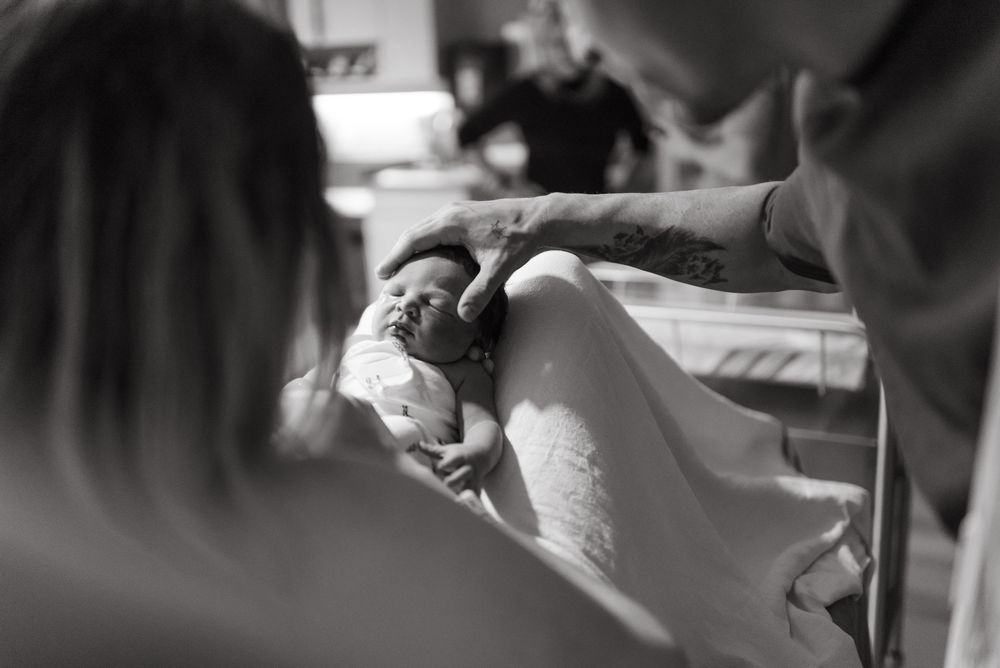 A newborn baby being cradled in a medical setting during labour captured in black and white photography.