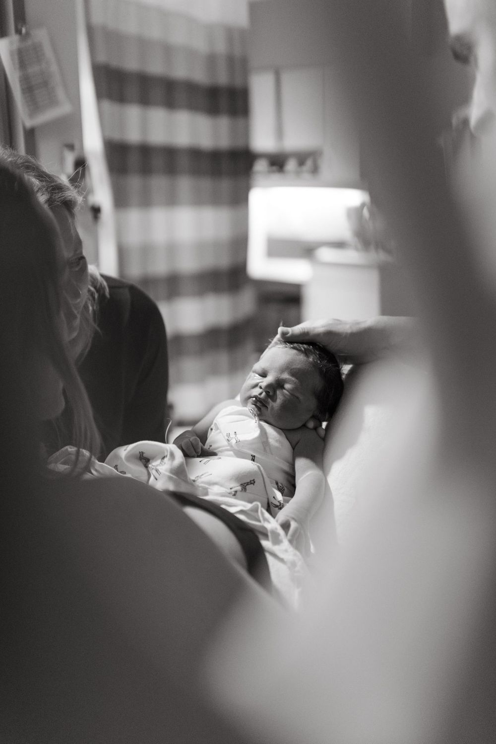 A tender black and white photograph captures a sleeping infant in soft light with blurred foreground elements.