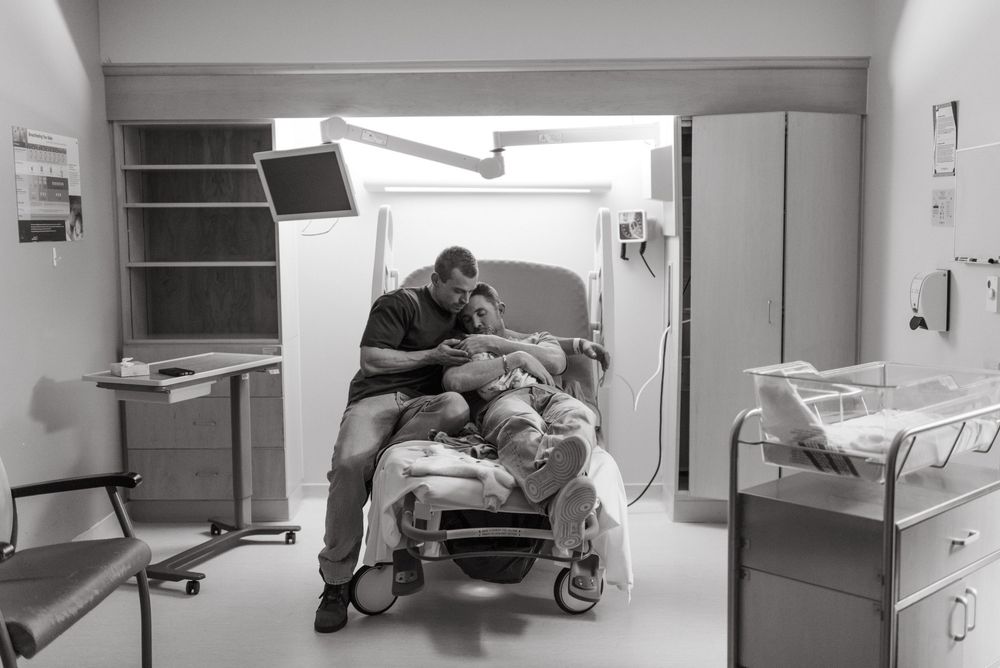 A hospital hallway shows a row of parked stretchers and medical beds along a wall in a dimly lit corridor.