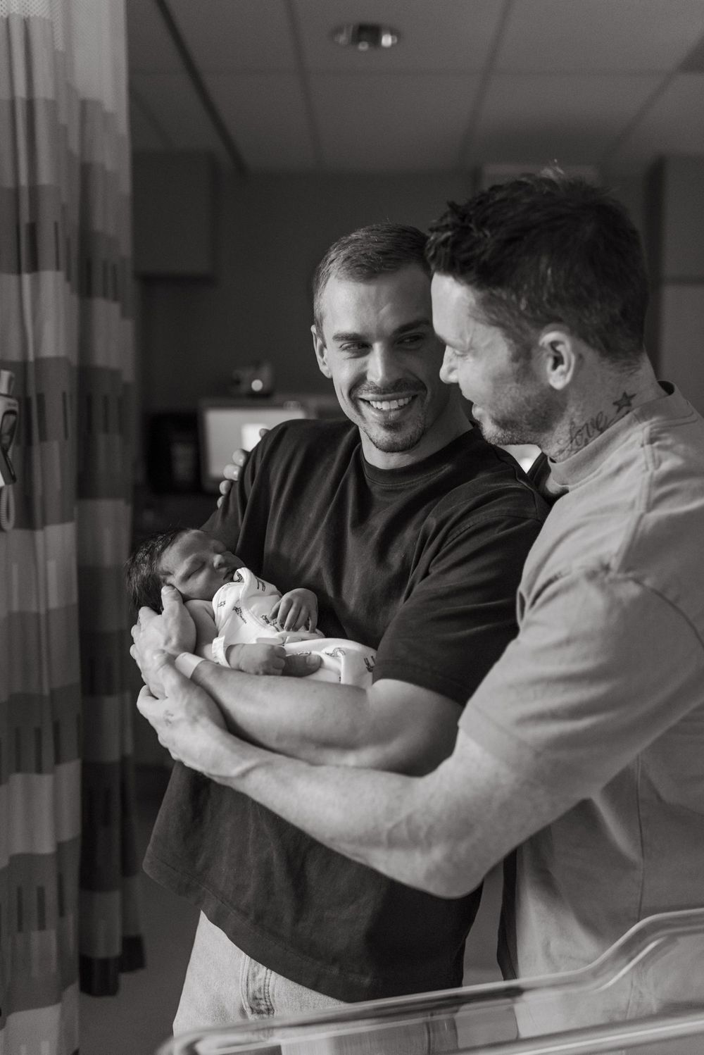 A black and white hospital photo showing two adults lovingly holding and gazing at a newborn baby.