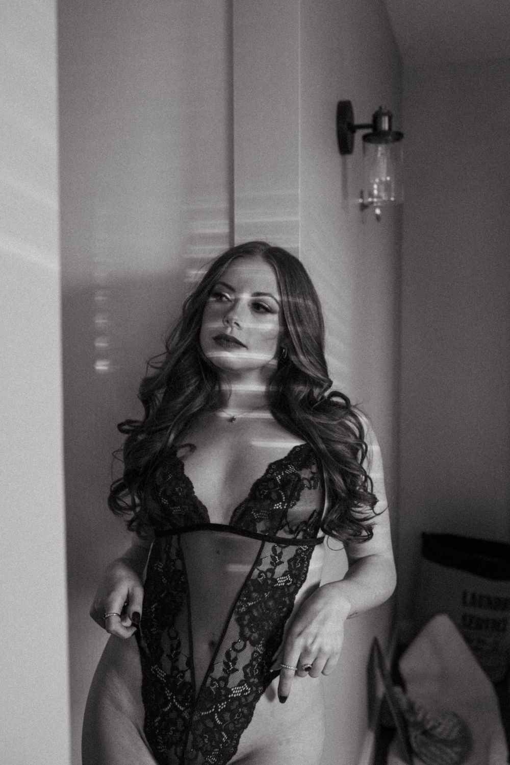 Black and white boudoir photo showing a figure in lace lingerie against a light background.