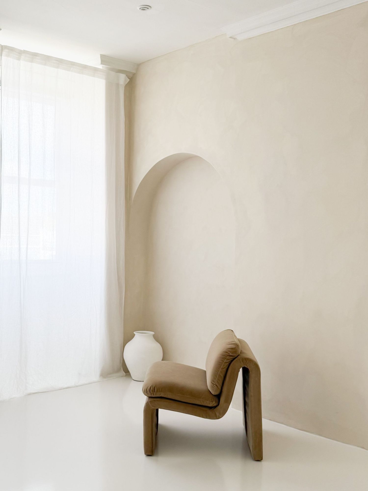 Minimalist white interior room with modern furniture and soft natural lighting through windows.
