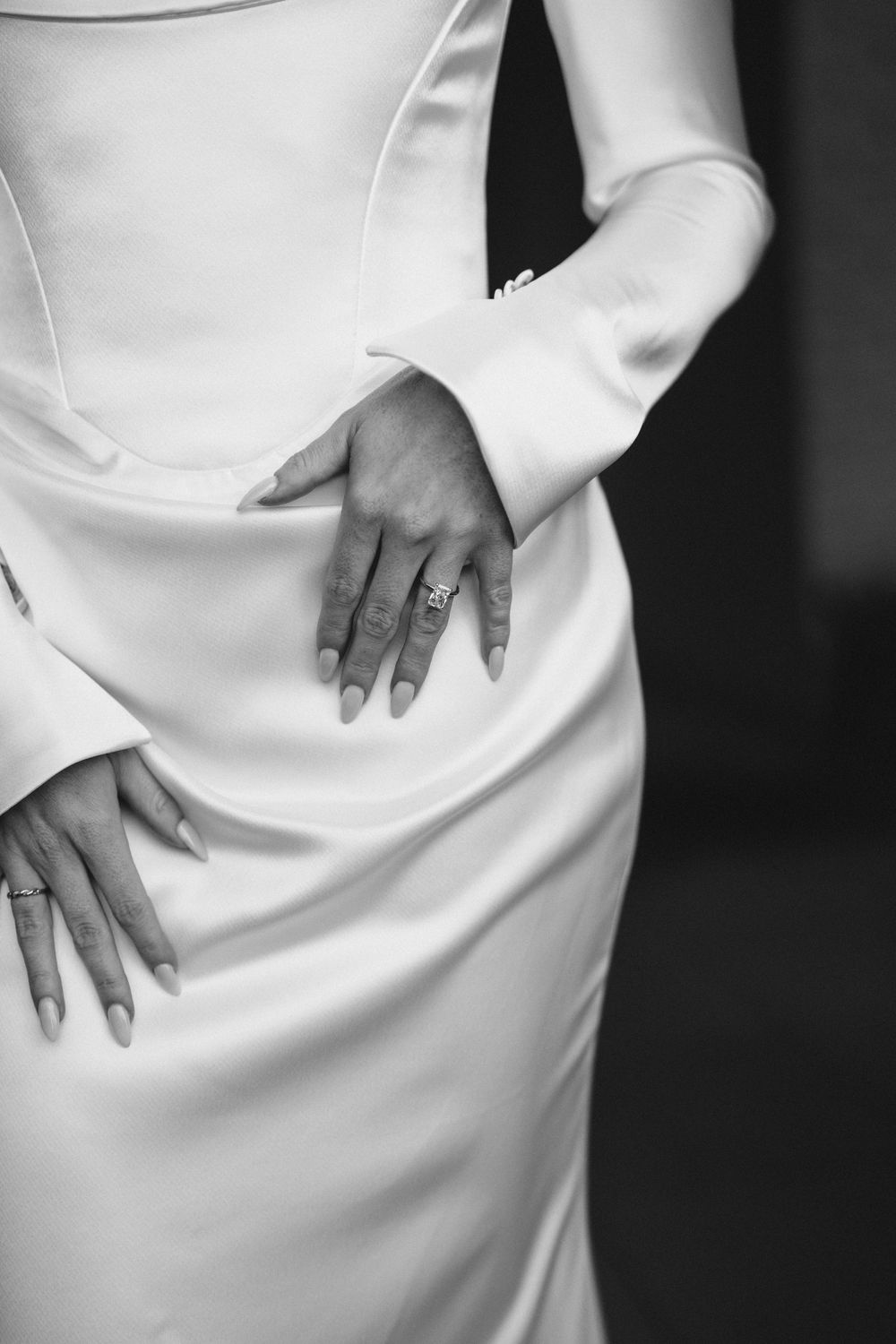 Close-up detail of hands resting against white fabric showing wedding rings and manicured nails.