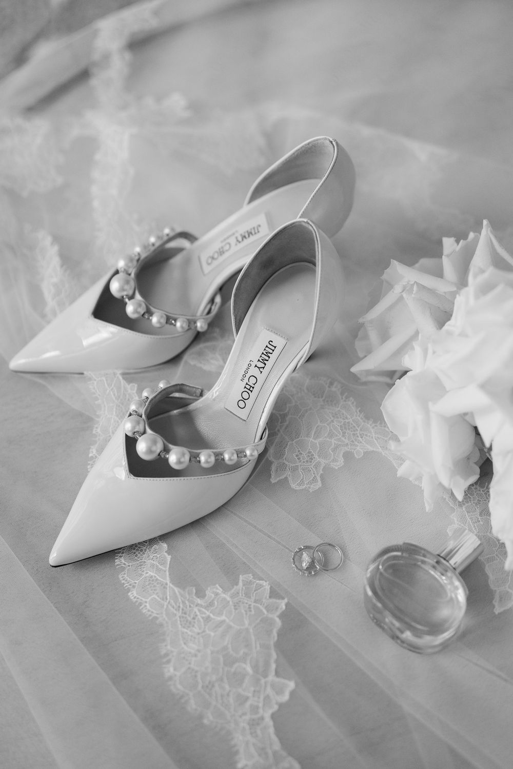 Elegant white pointed-toe bridal shoes with pearl details displayed alongside delicate lace and wedding accessories.