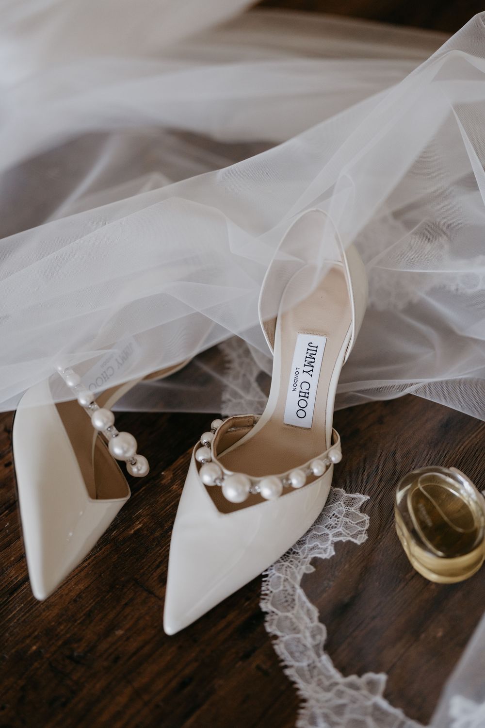 Elegant white bridal shoes with pearl details displayed with delicate veil on wooden surface.