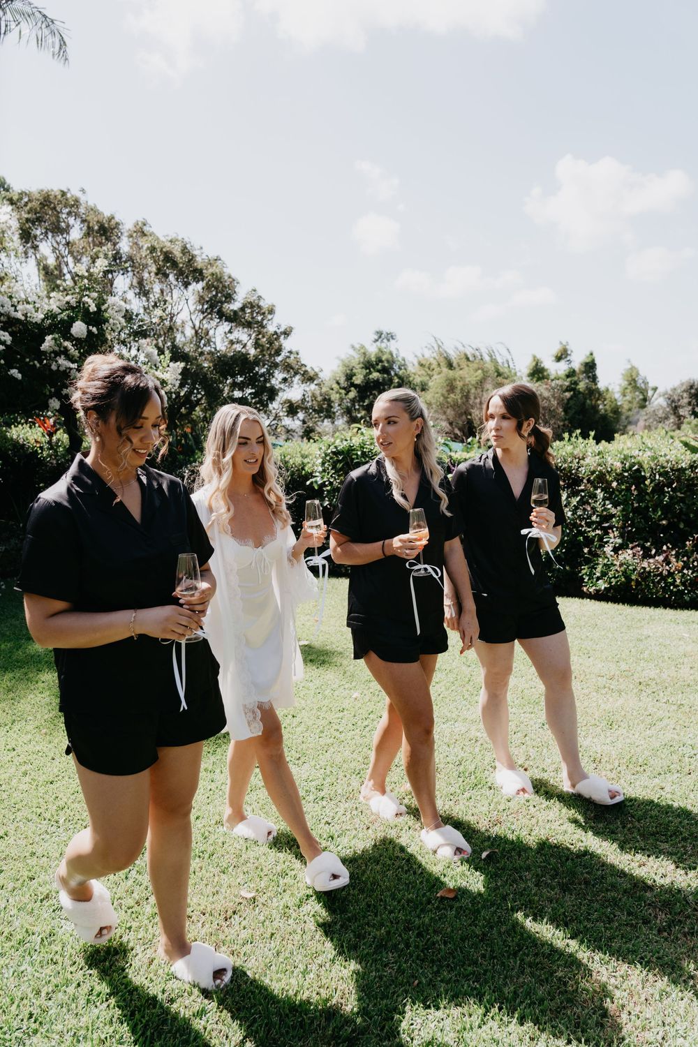 Wedding party in black and white outfits posing playfully on sunny lawn.