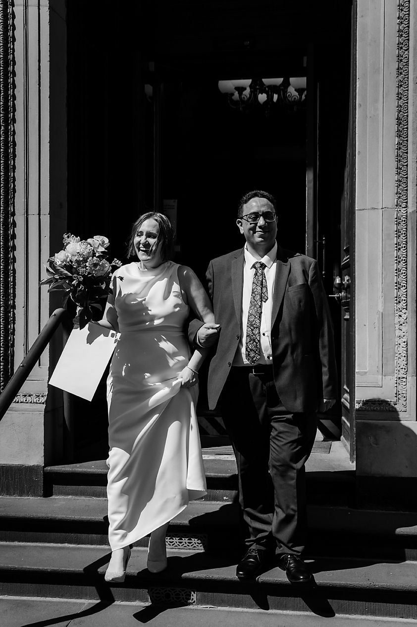 A candid black and white image capturing wedding guests walking on a sunlit sidewalk.