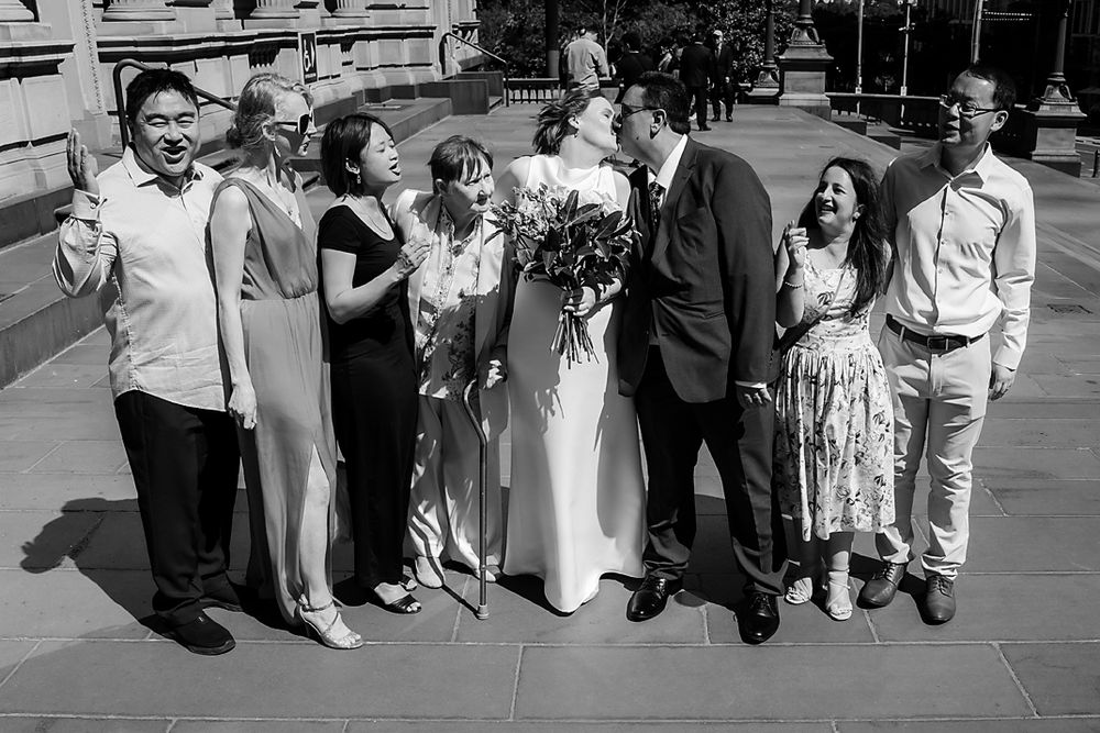 Wedding party members lined up outdoors for a group photo on a bright sunny day.