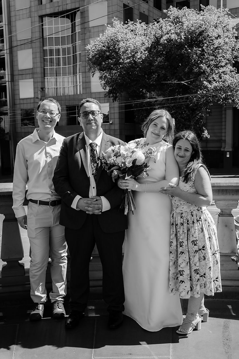 A black and white wedding party photo standing outside a building with flowering trees in spring.