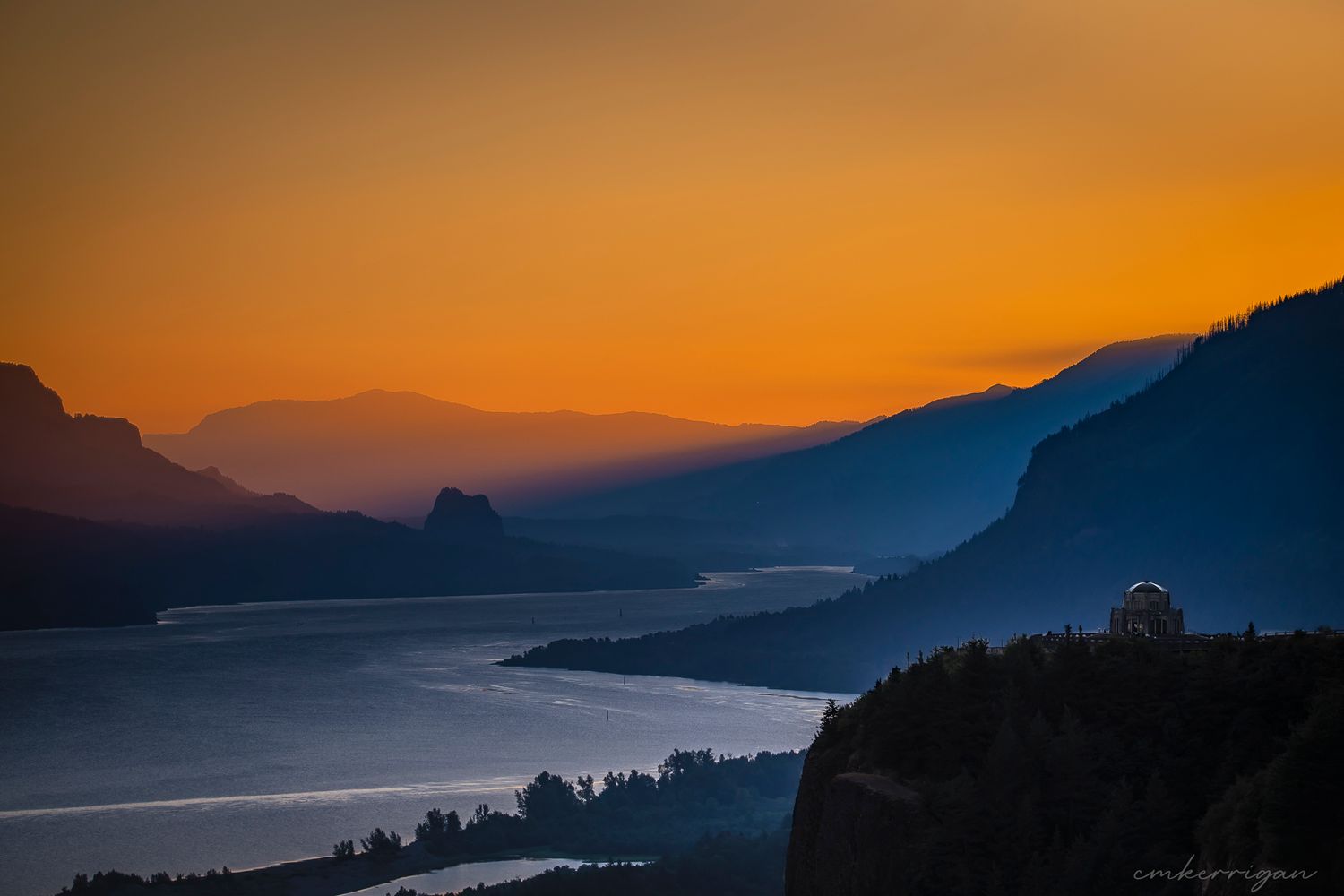 Golden sunset silhouettes mountains against an orange sky over the Columbia River.