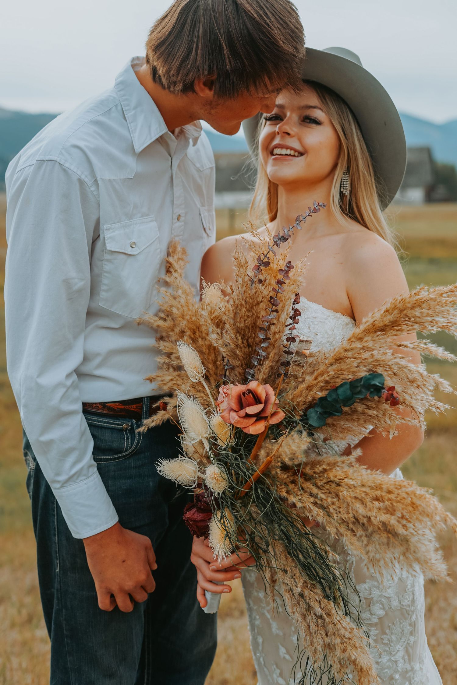 Romantic western-themed couple with dried flower bouquet in mountain setting.