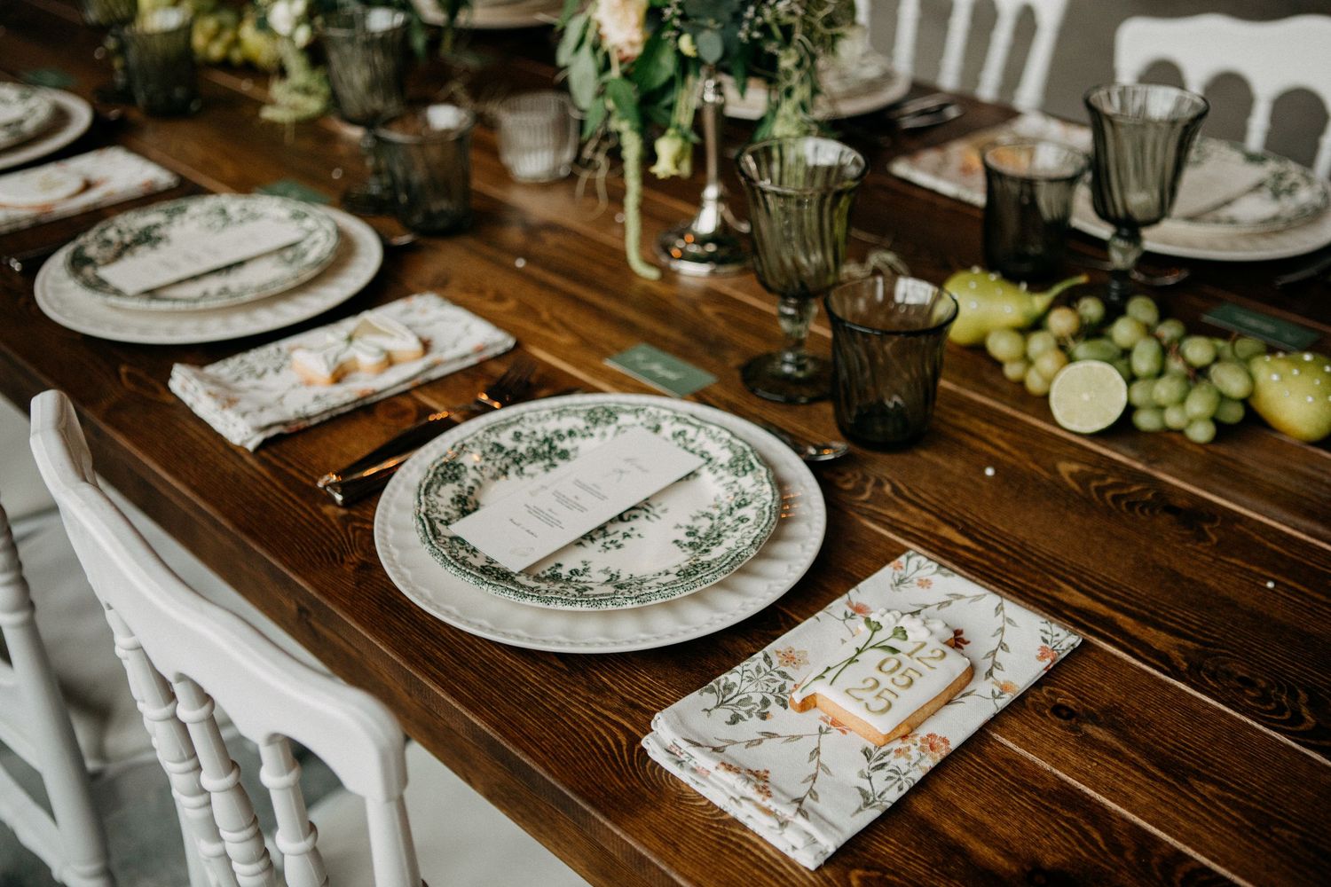 Elegant rustic wedding reception table set with green floral plates, patterned napkins, and fresh fruit centerpiece.