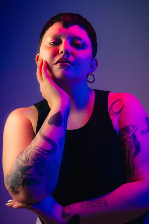 Artistic portrait series in neon pink and blue lighting showing a figure with tattoos striking dramatic poses against dark background.