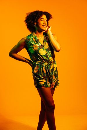 Fashion model in tropical print outfit poses dynamically against vibrant orange background in photo series.