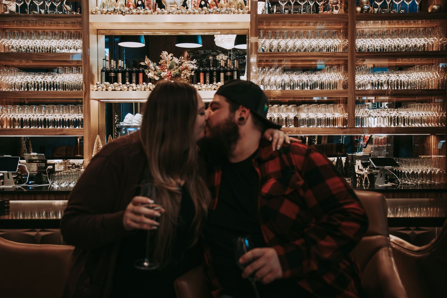 People enjoying drinks at a dimly lit bar with an extensive wall of spirits and glassware in the background.