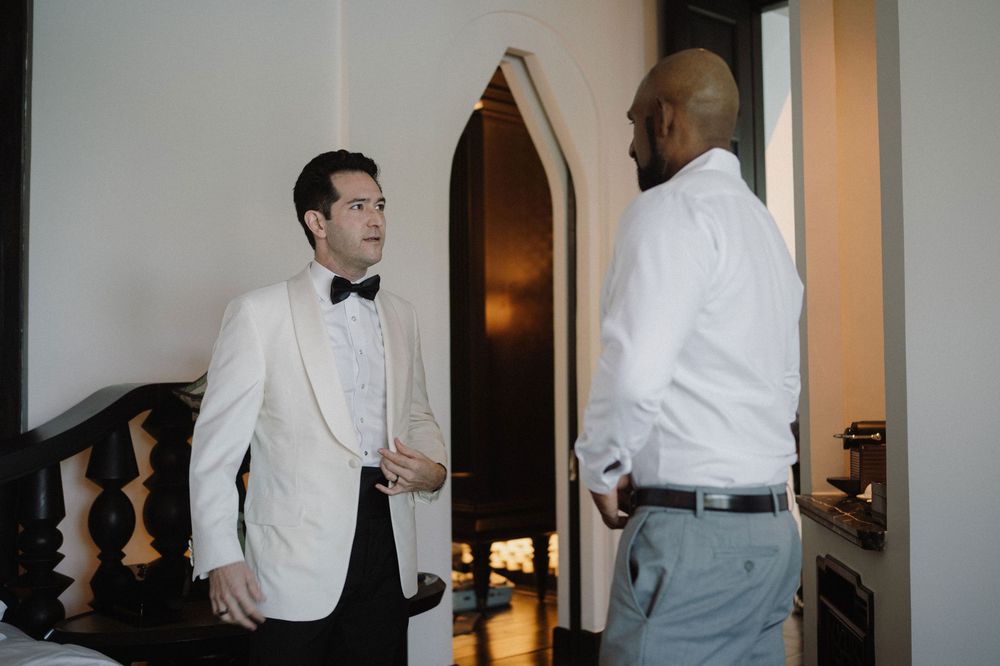 Group of men getting ready in a hotel room wearing formal white dress shirts and bow ties.