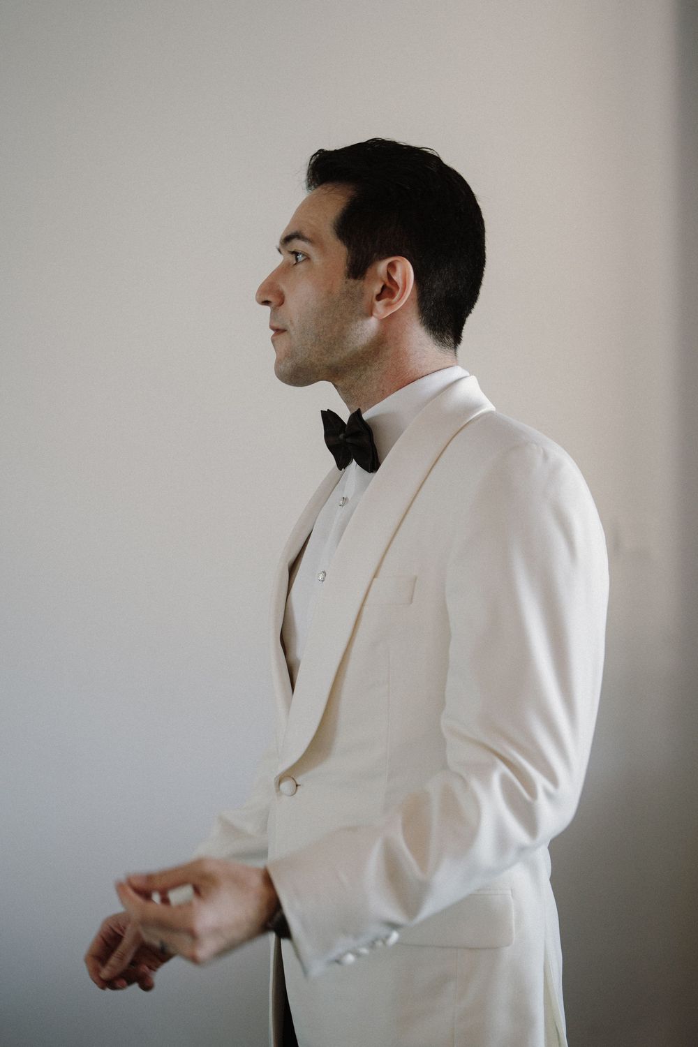 Multiple shots of person in white tuxedo jacket and bow tie getting ready against neutral background.