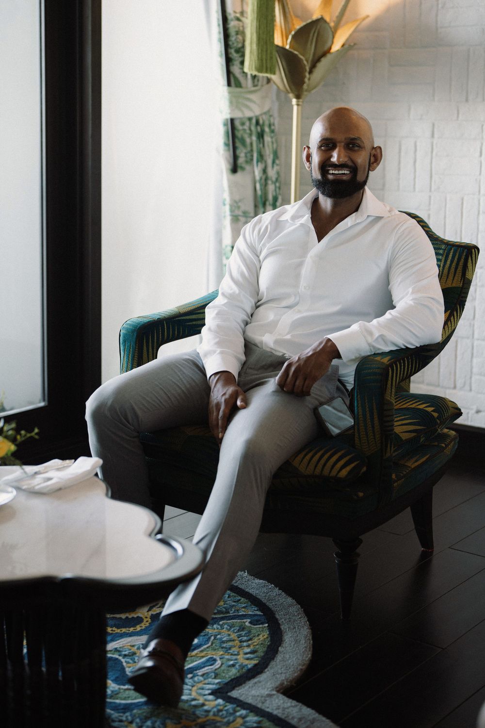 Person in white shirt seated on teal patterned chair in modern interior setting with natural lighting.