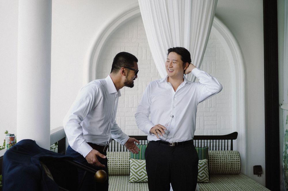 Wedding party members in white shirts preparing in an elegant room with arched columns.