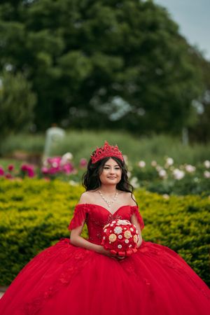 A stunning red quinceañera dress with a sweetheart neckline and full tulle skirt photographed in a garden setting.