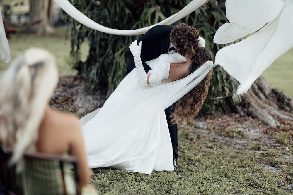 Elegant outdoor wedding decor with white draping fabric hung between trees creates a romantic garden ceremony setting.