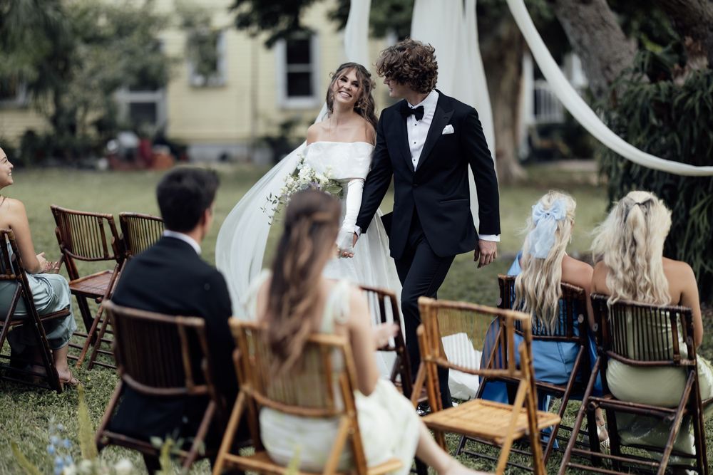 Outdoor wedding ceremony setup with wooden chairs arranged on grass under flowing white fabric canopy.