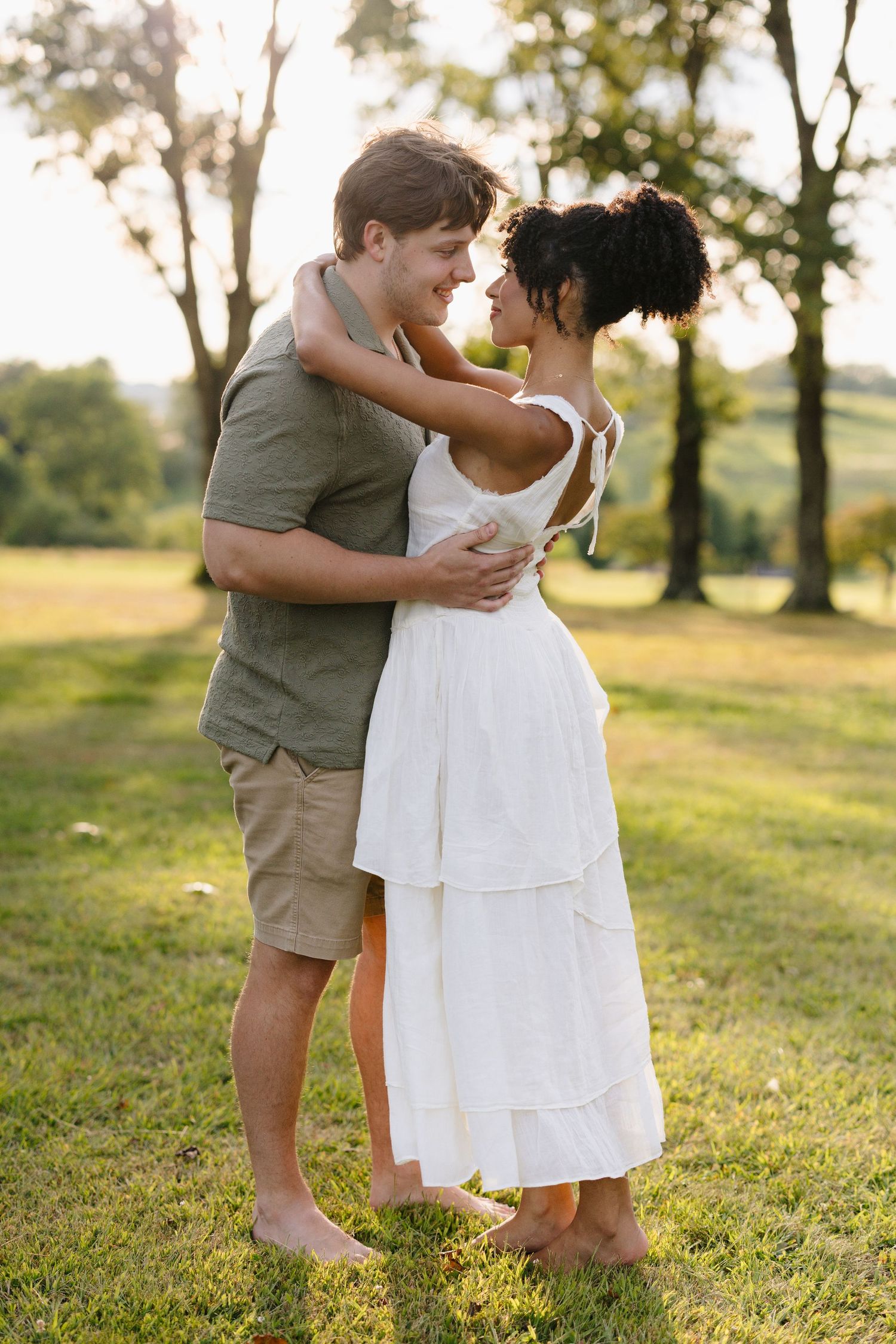 Candid moments captured between a couple in white and tan outfits on a grassy hillside.