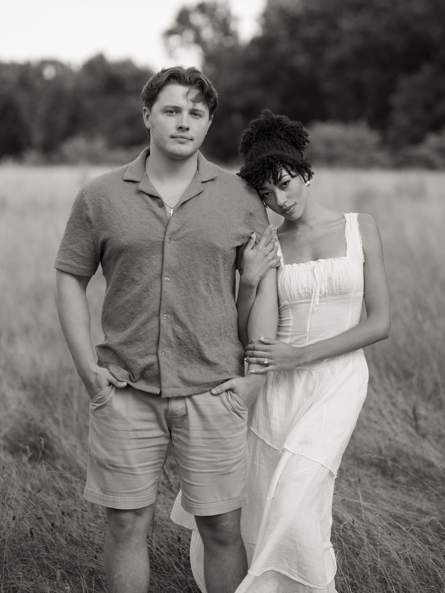 Black and white portrait of a couple embracing in a rustic outdoor field setting.