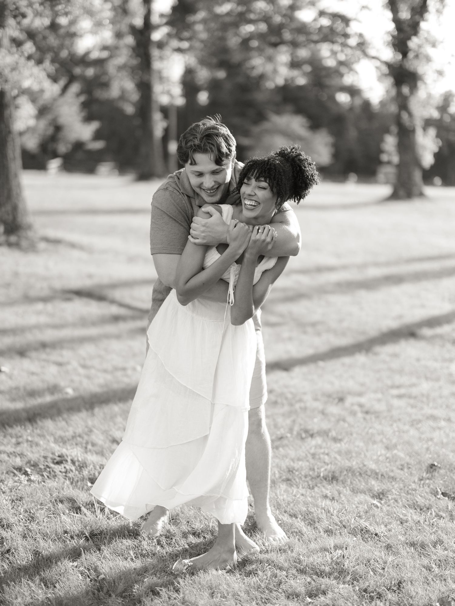 A couple in casual attire shares laughter and affection while playing in a grassy field.