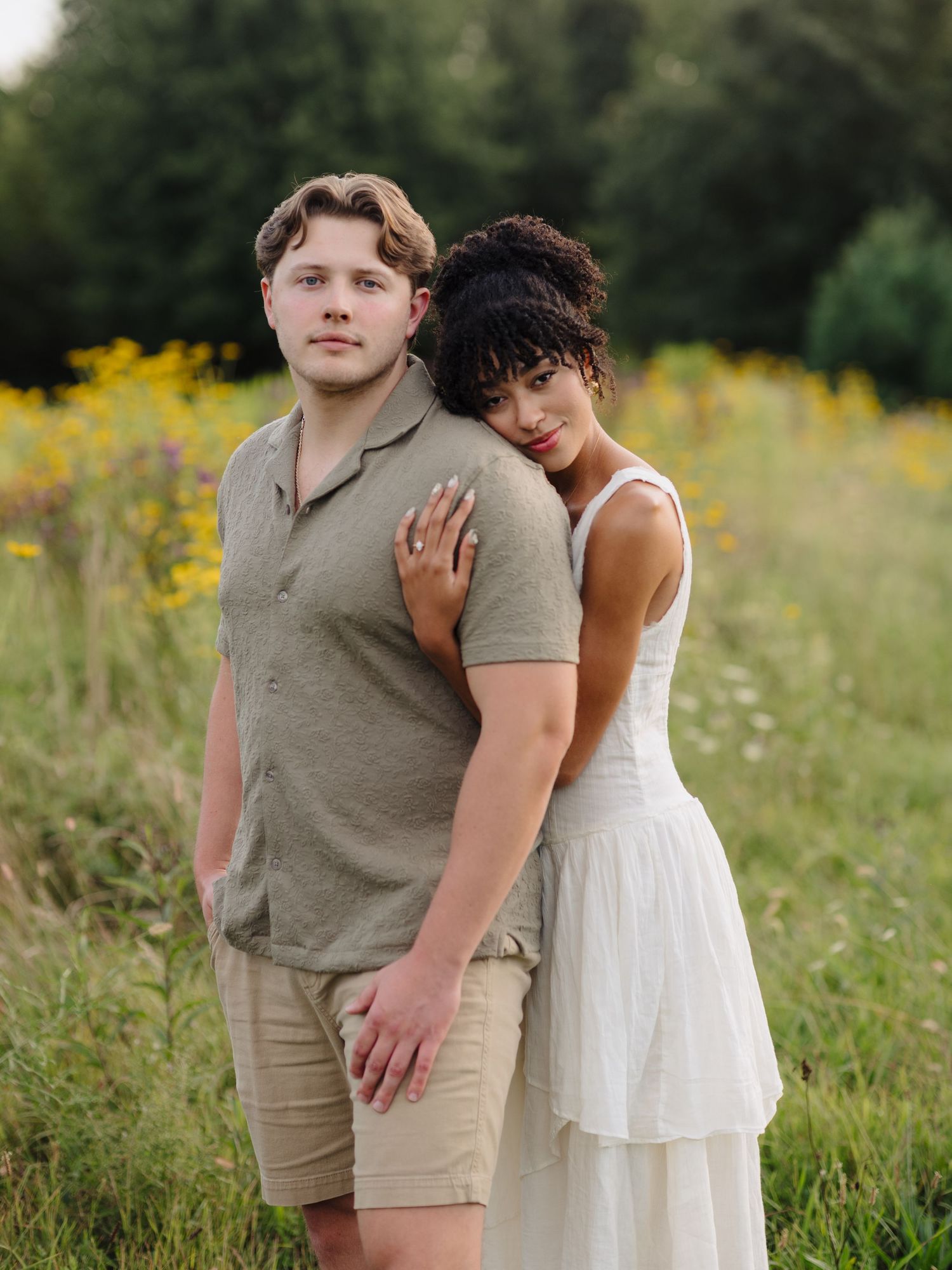 A couple poses together in a field of yellow wildflowers during golden hour.
