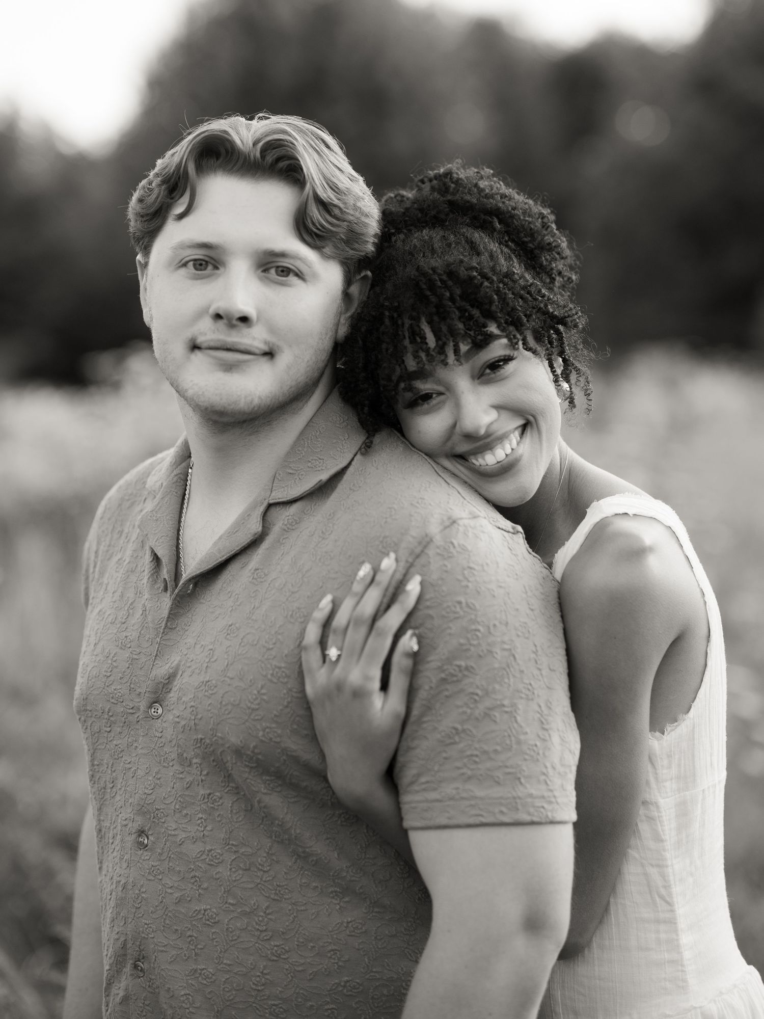 A black and white portrait of a couple smiling and embracing outdoors.