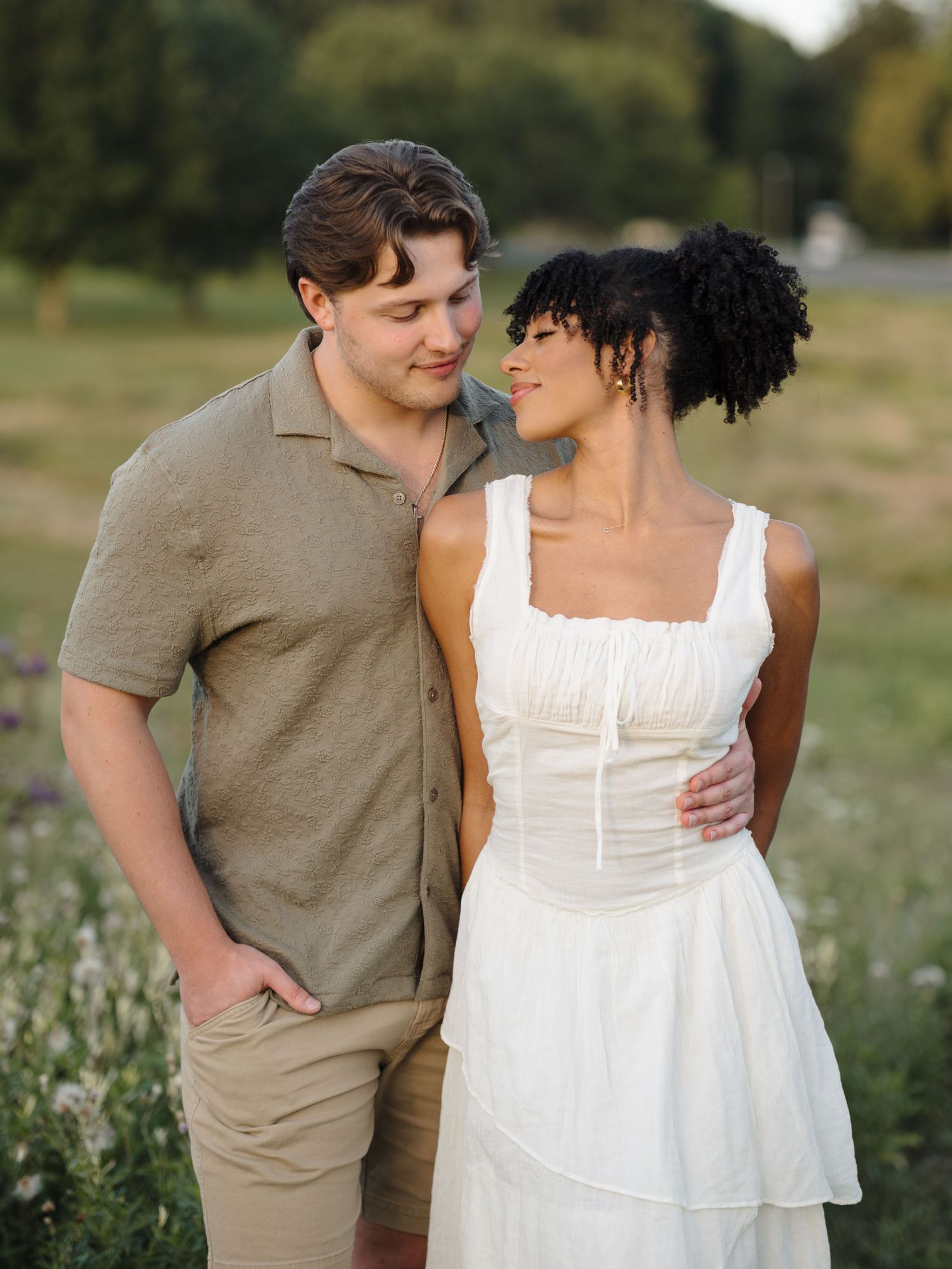A couple shares intimate moments in a field during a summer photoshoot.