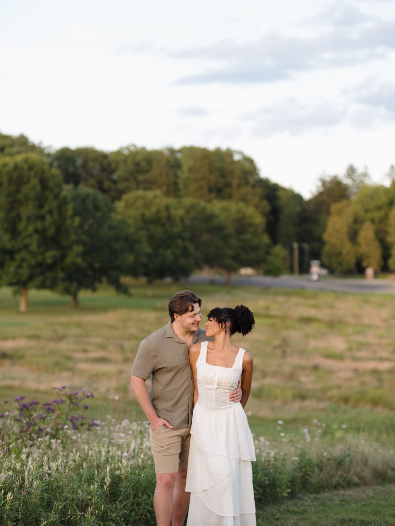 Couple shares tender moments in a wildflower field during a summer evening photoshoot.