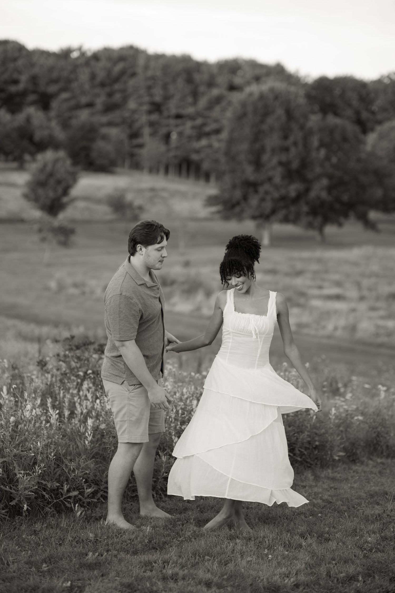 Couple in casual attire plays with a white dress together in a scenic meadow landscape.