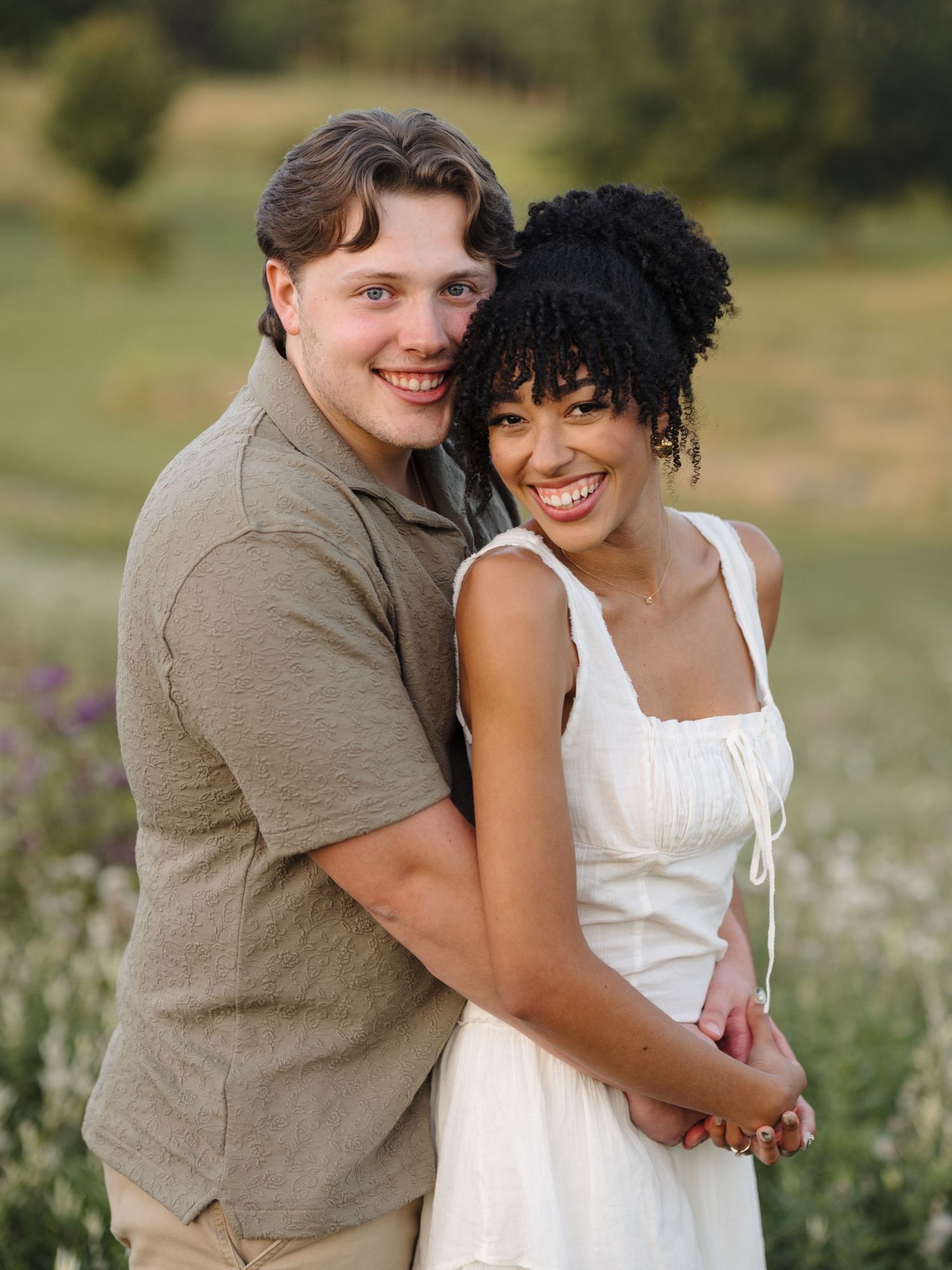 A couple embraces and laughs together in a summer field with wildflowers.
