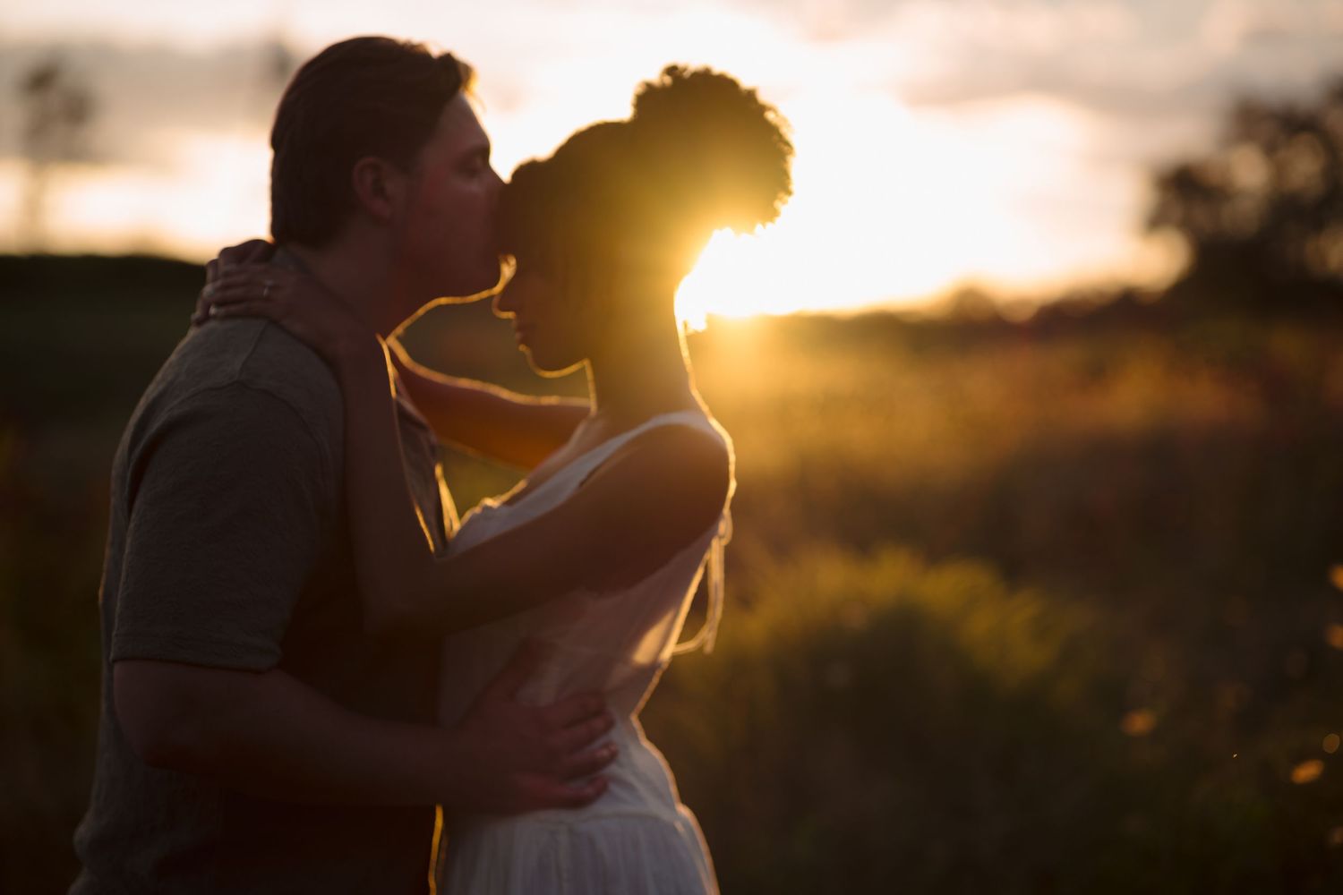 Romantic silhouette of two people sharing an intimate moment at dusk with warm sunlight behind them.