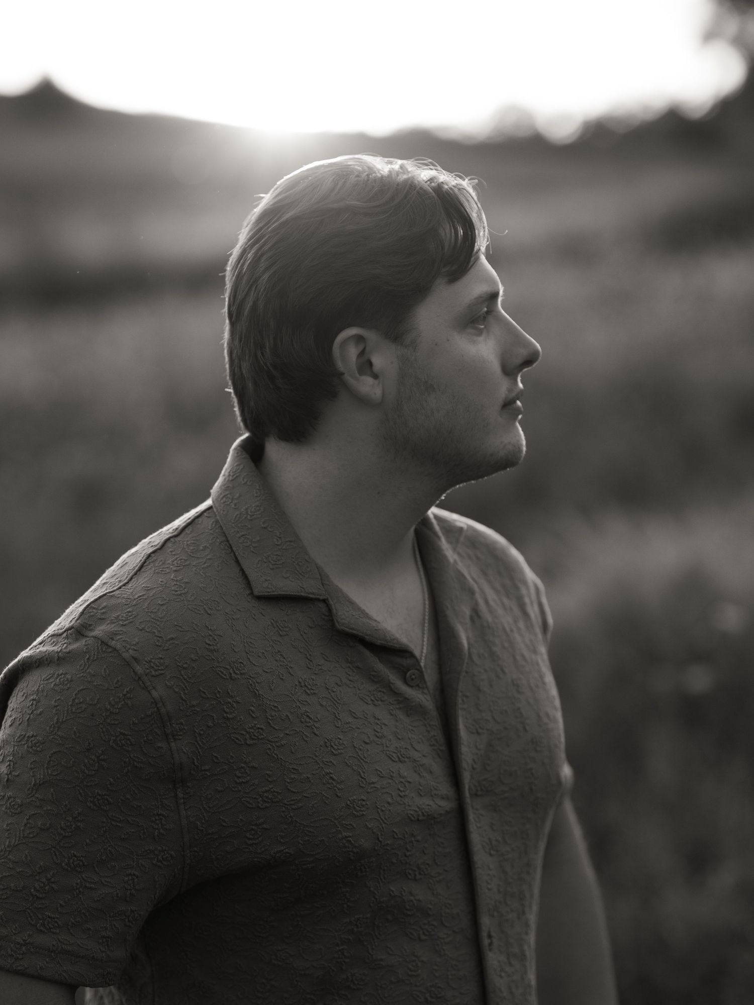 Black and white profile portrait showing contemplative gaze toward the sky in moody lighting.