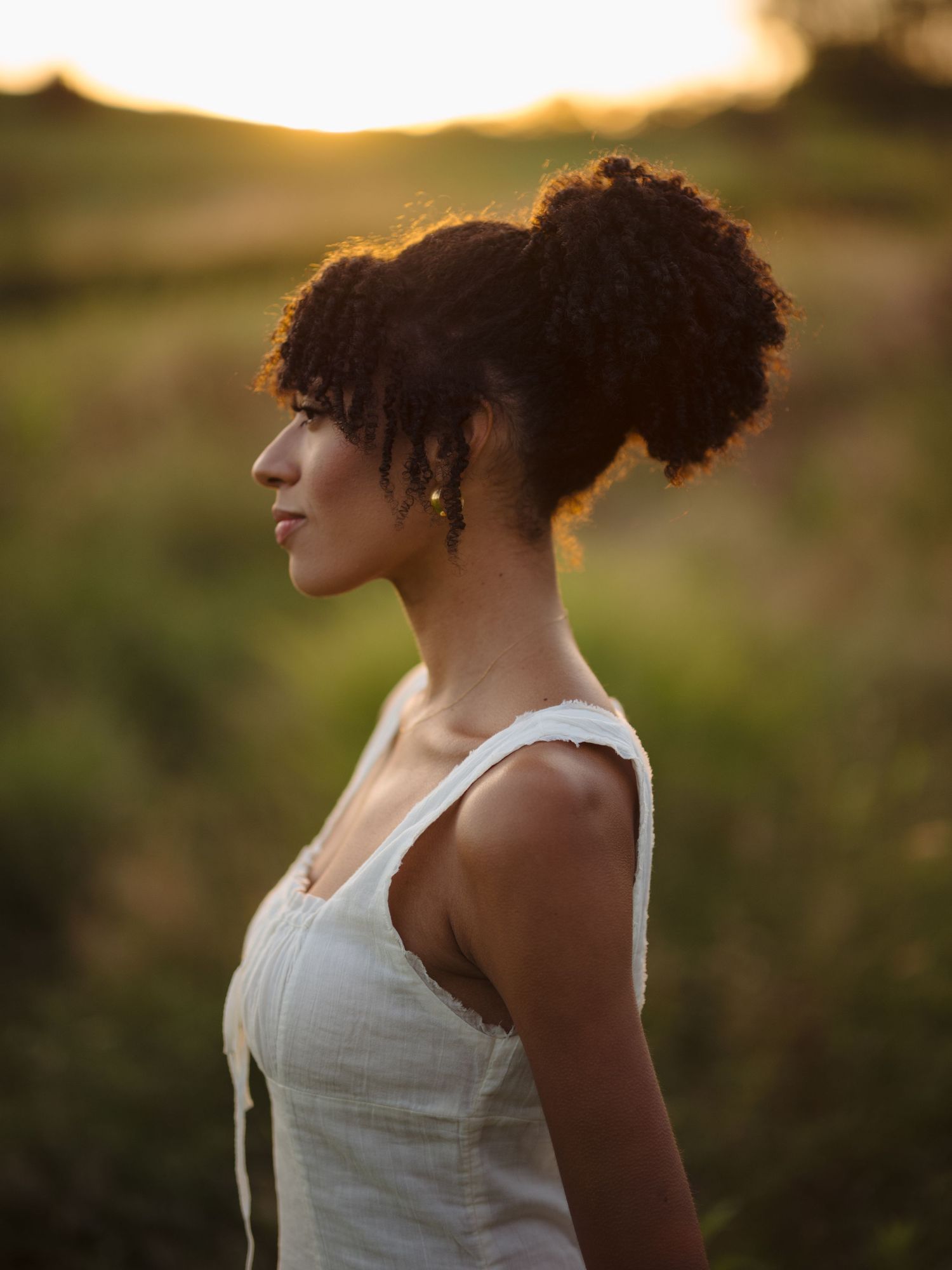 Silhouette of person with curly hair in white top against golden sunset.