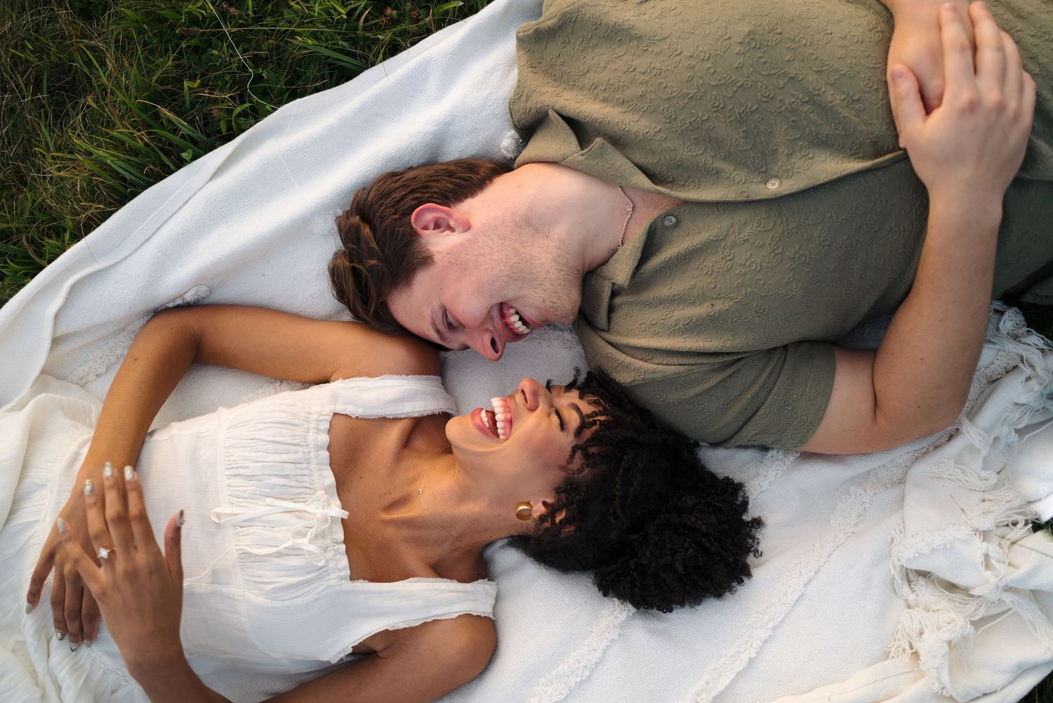 Romantic couple lying together in a grassy field in tender embraces, sharing intimate moments.