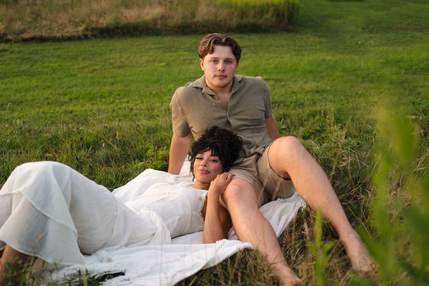 A romantic couple embraces while lying in a grassy meadow on a sunny summer day.